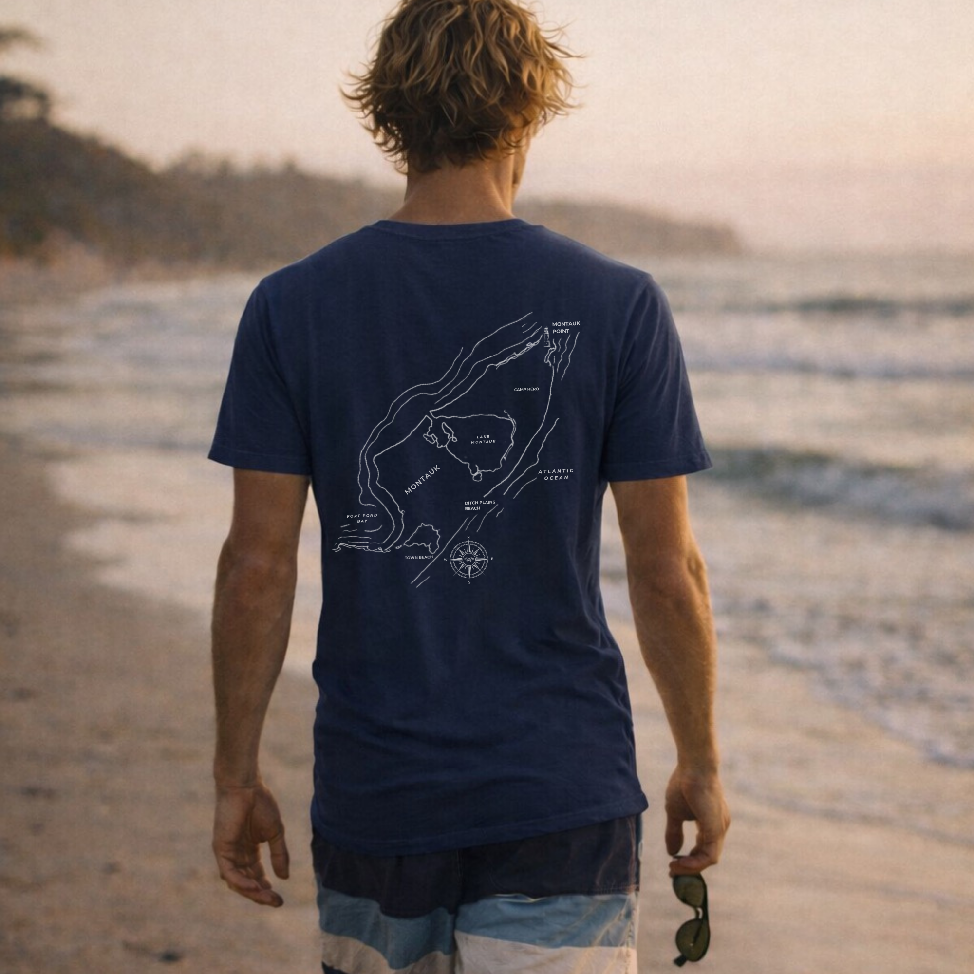 Man wearing coastal navy blue short sleeve t-shirt with map of Montauk, NY on the back and gps coordinates of Montauk on the front.